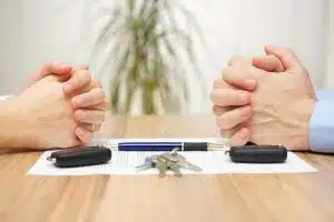 Two people with folded hands on a divorce decree with keys in the middle.